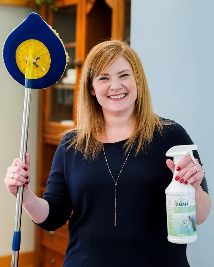 Woman smiling while holding a spray bottle of household cleaner and a round-headed mop