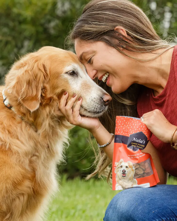 Woman touching foreheads with a golden retriever while holding a bag of Nala's dog treats