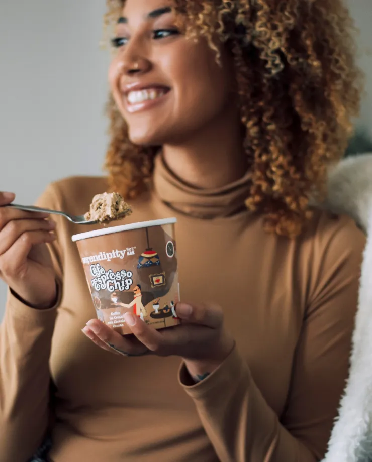 Woman with curly hair smiling as she eats from a pint of Serendipity ice cream