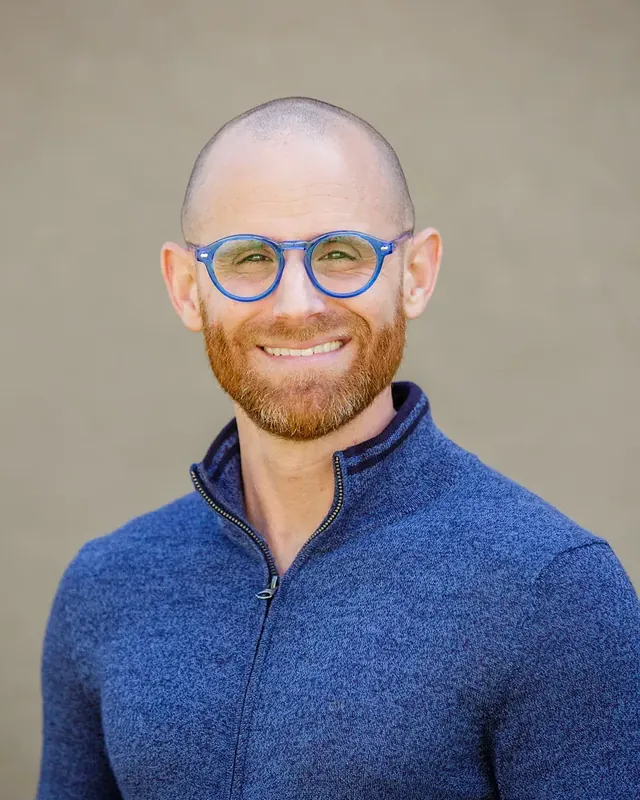 Cory Warren, CEO of C4 Social, smiling in round blue glasses and a zip-up sweater