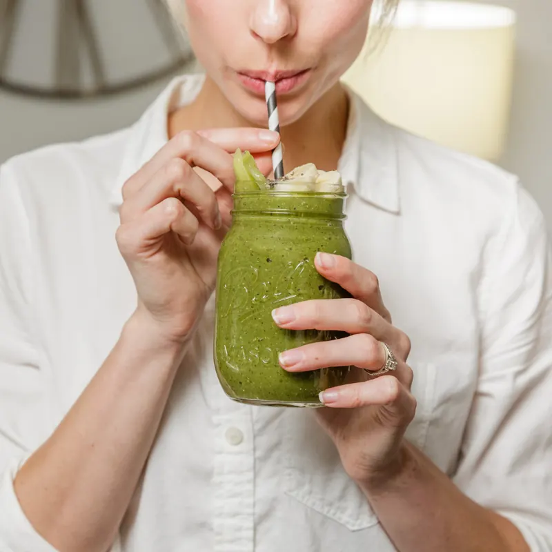 Woman sipping a green smoothie through a striped straw from a glass jar