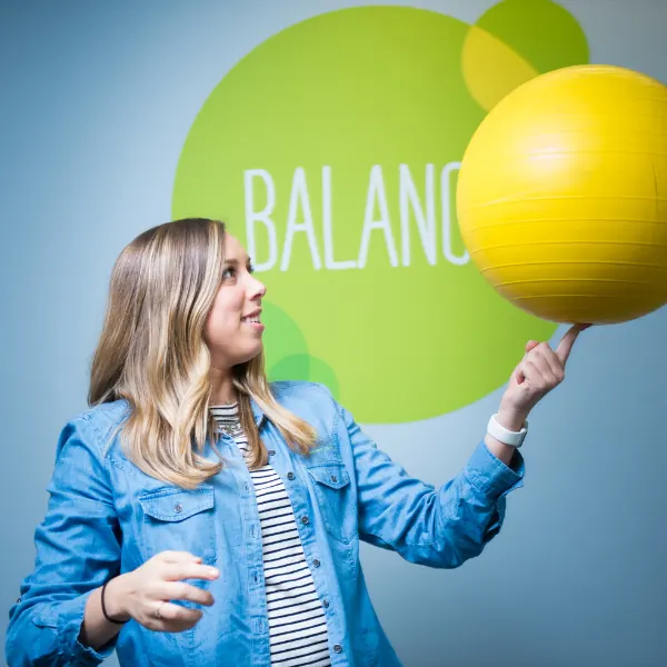 Coach in a denim jacket spinning a yellow ball on her finger in front of a wall that reads BALANCE