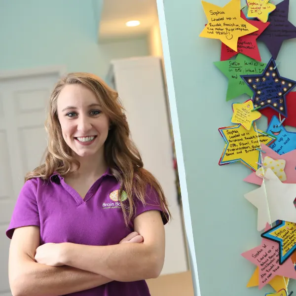 Brain Balance coach in a purple polo smiling beside a wall of handwritten paper stars