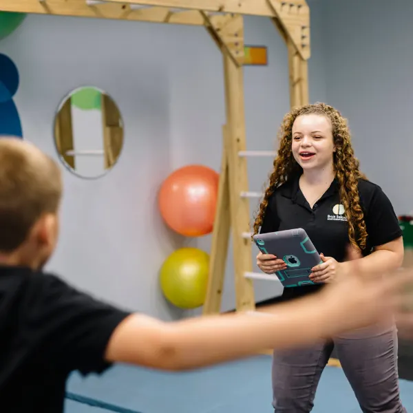 Coach smiling and holding a tablet as a boy works through an exercise in the gym