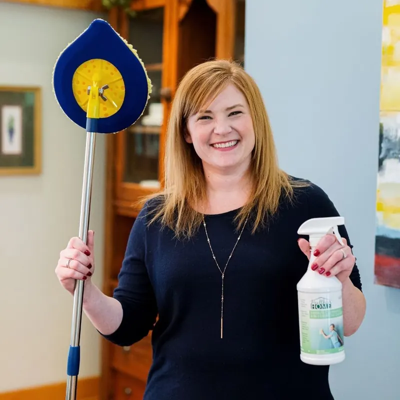 Woman smiling as she holds a round-headed mop and a Healthier Home spray bottle