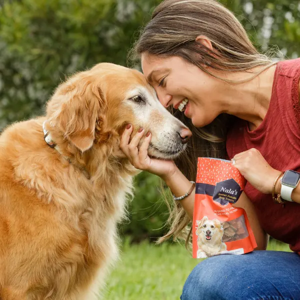 Woman hugging a golden retriever while holding a bag of Nala's dog treats