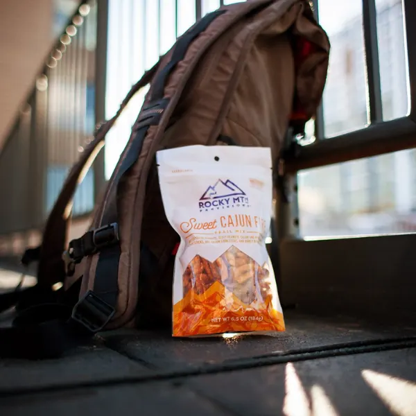 Bag of Rocky Mtn trail mix next to a backpack by a sunny window