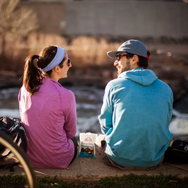 Couple sitting by a river sharing a bag of trail mix