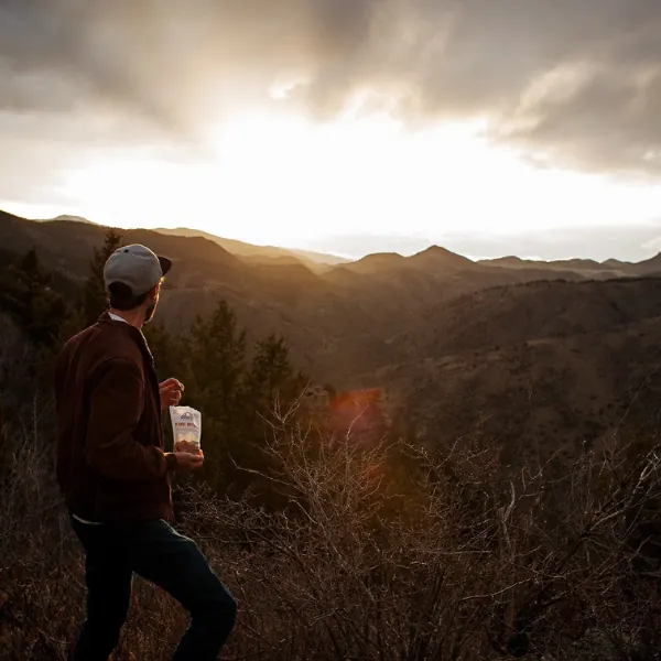 Hiker on a mountain ridge at sunset holding a bag of trail mix