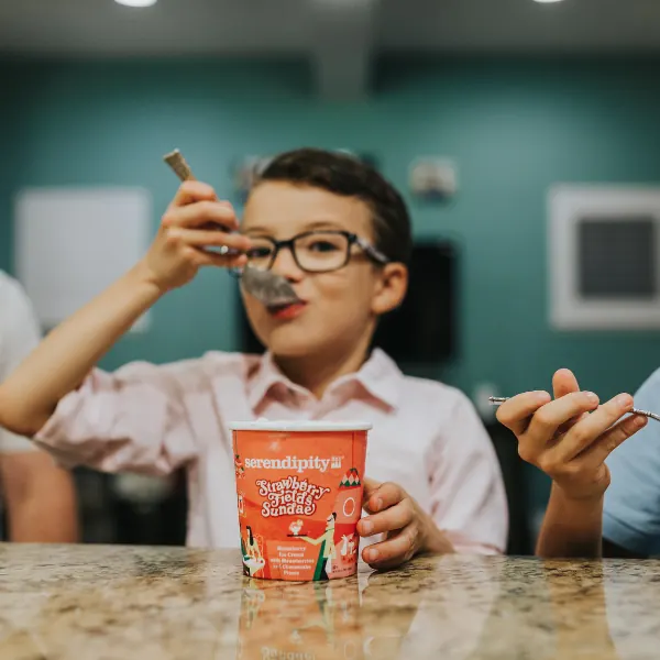 Boy in glasses tasting a spoonful of Serendipity ice cream at a counter