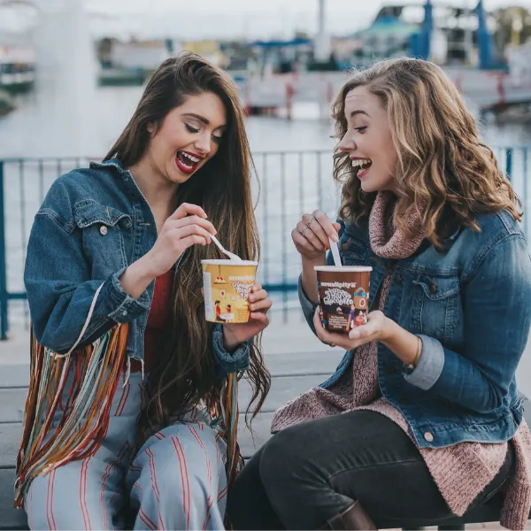Two friends laughing as they eat pints of Serendipity ice cream by the waterfront