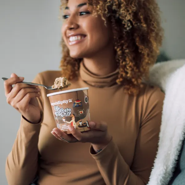 Woman with curly hair smiling as she eats from a pint of Serendipity ice cream
